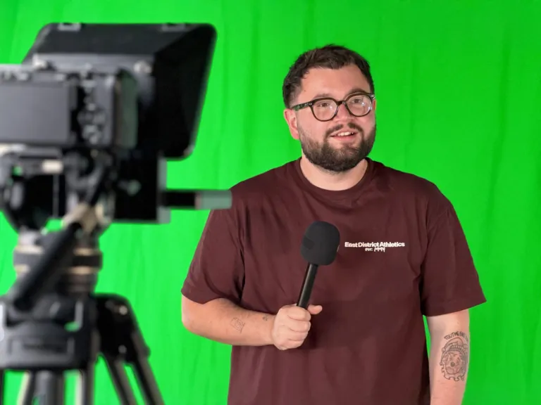 Présentateur au micro devant le fond vert, prompteur au premier plan